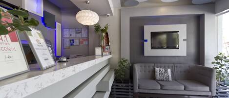 A modern reception area with a marble counter, a grey sofa, and a mounted TV.