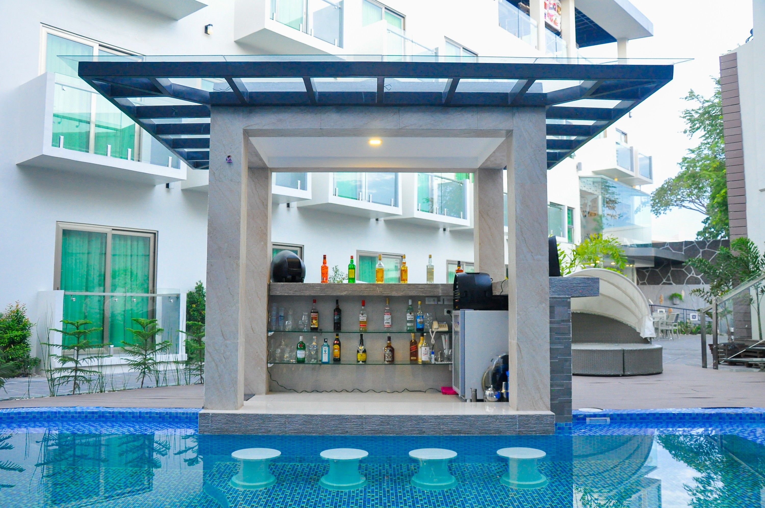 Um bar de hotel moderno com vista para a piscina, apresentando um guarda-corpo de vidro, diversas garrafas e uma área de estar.