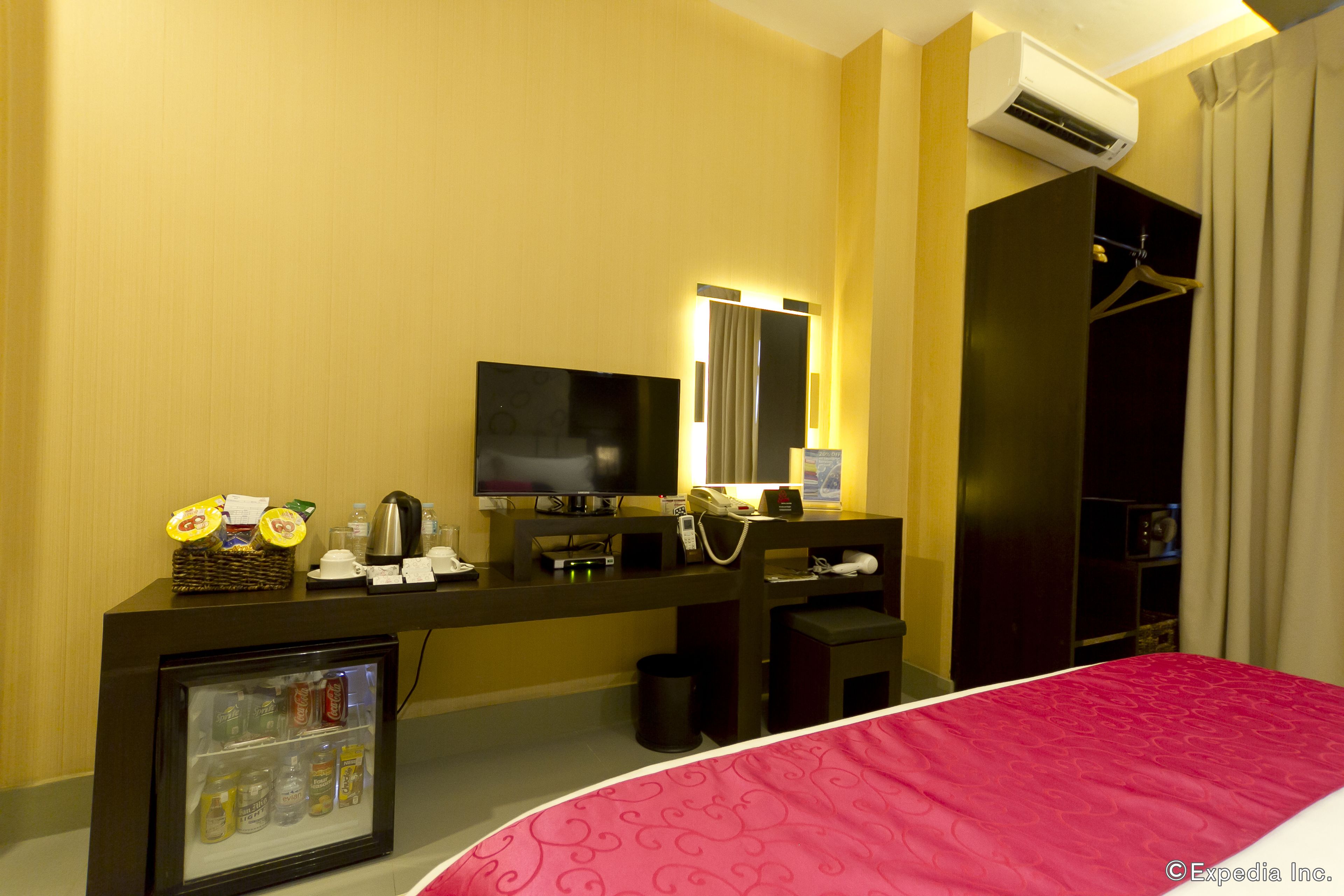 Habitación de hotel con cama, televisión, minibar, espejo y armario.