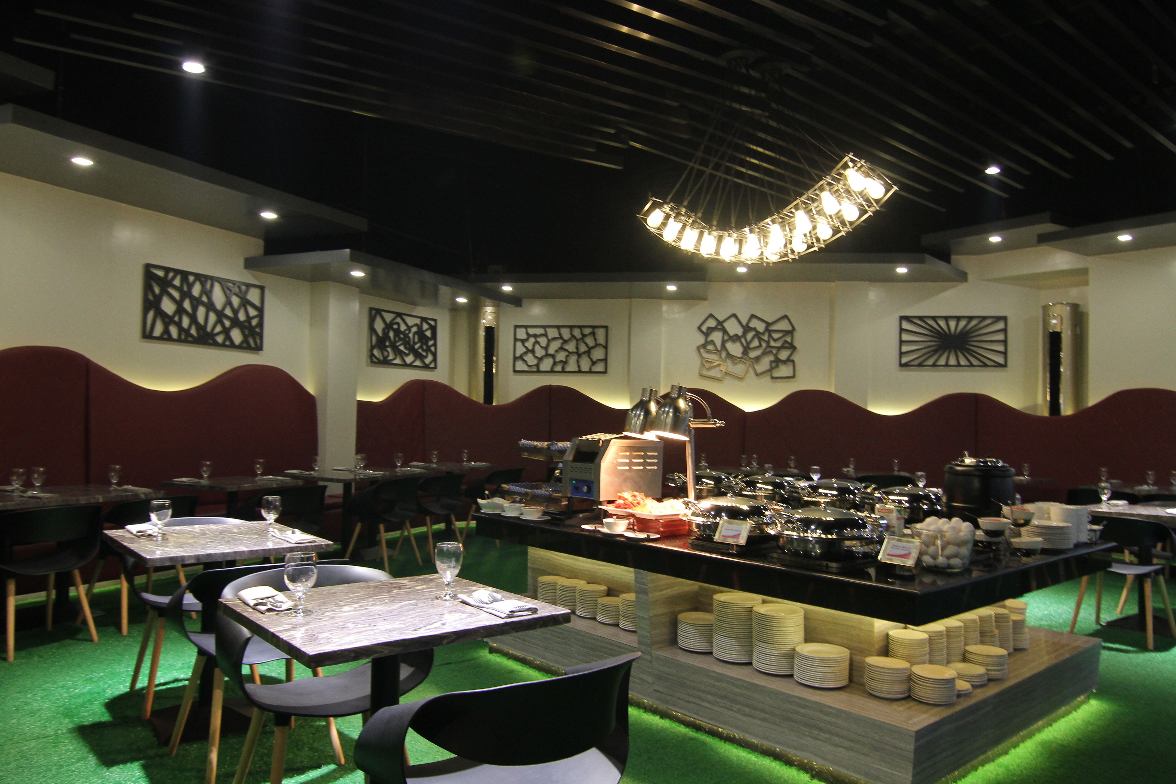 A restaurant with tables and chairs, a buffet area with plates and bowls, and decorative wall art.