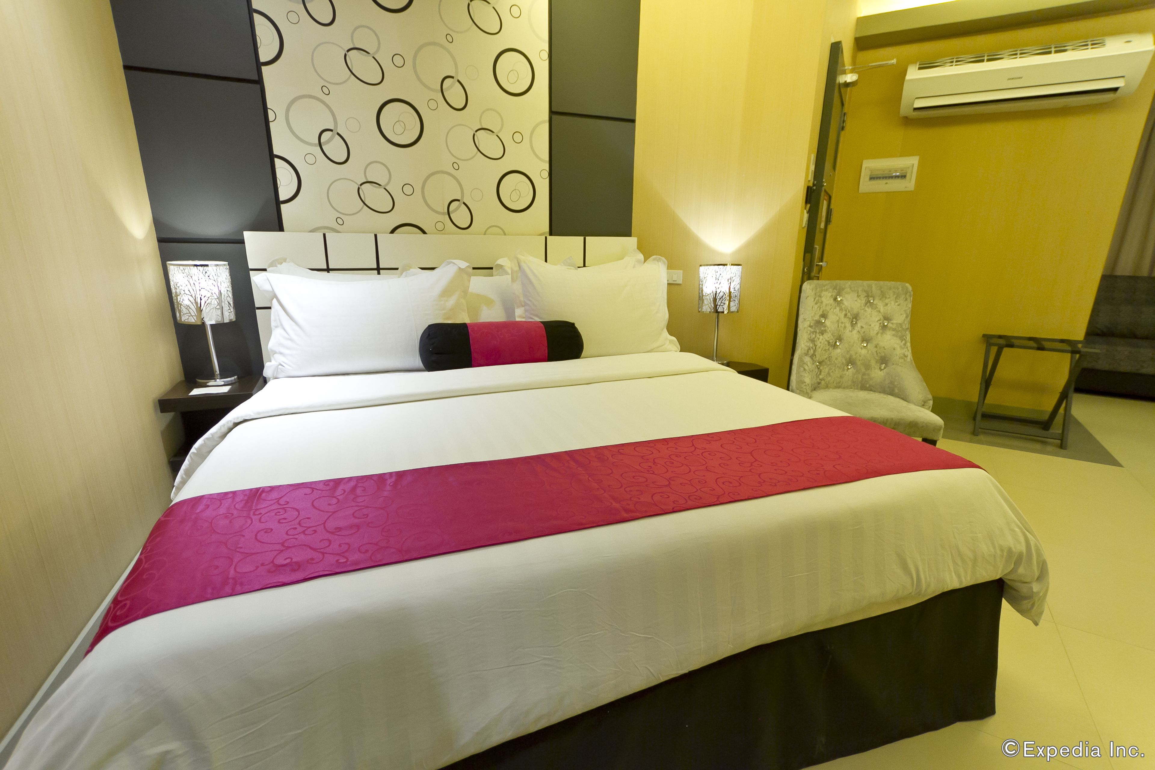 A hotel room with a large bed, a chair, an air conditioning unit, and a wall with a circular pattern.