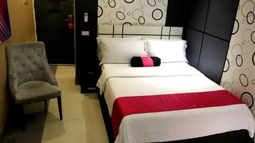 A hotel room with a bed, a grey upholstered chair, and a patterned wall.