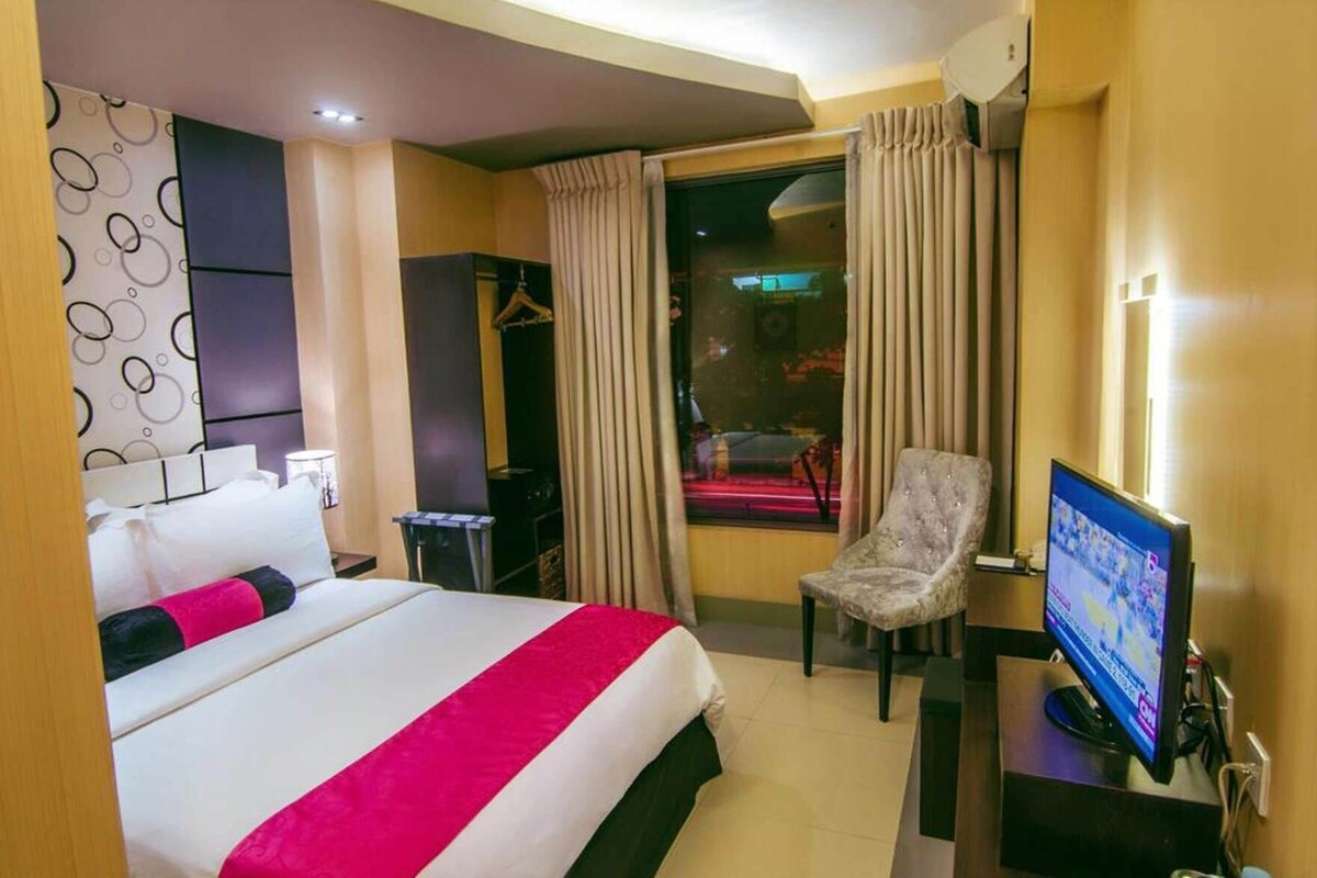 A hotel room with a bed, a chair, a TV, and a window with curtains.