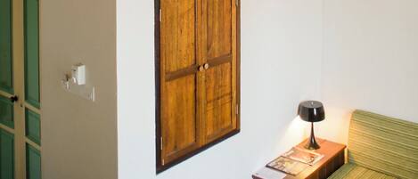 A bunk bed with a wooden headboard, a green door, a wooden cabinet, and a bedside table with books and a lamp.