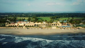 Un complejo turístico frente al mar, con palmeras y un campo de golf al fondo.