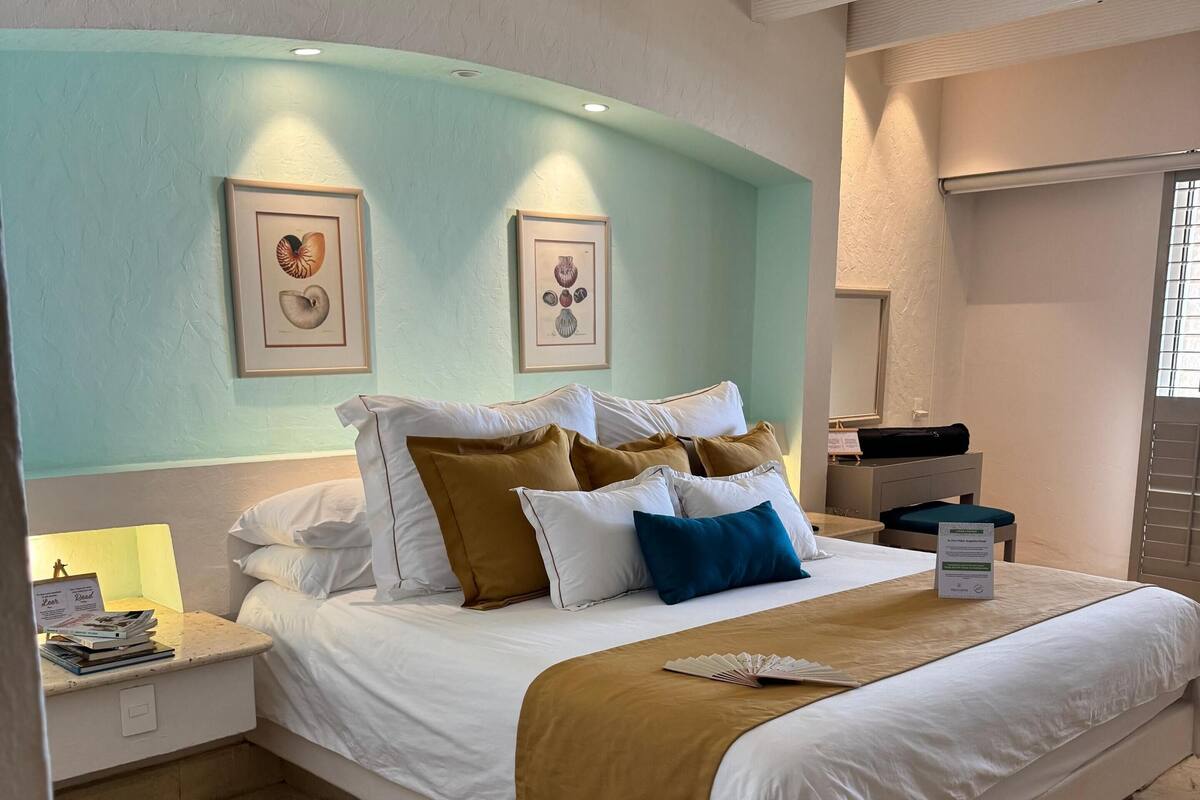 Een moderne hotelkamer met een groot bed, een nachtkastje, een raam met zonwering en een ingelijst schilderij aan de muur.
