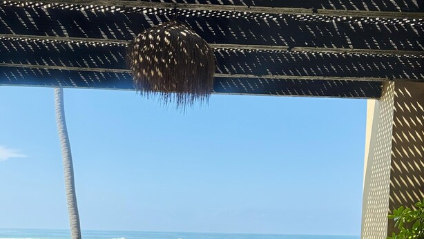 Vista a la playa desde un espacio techado con sillas de descanso y una mesita.