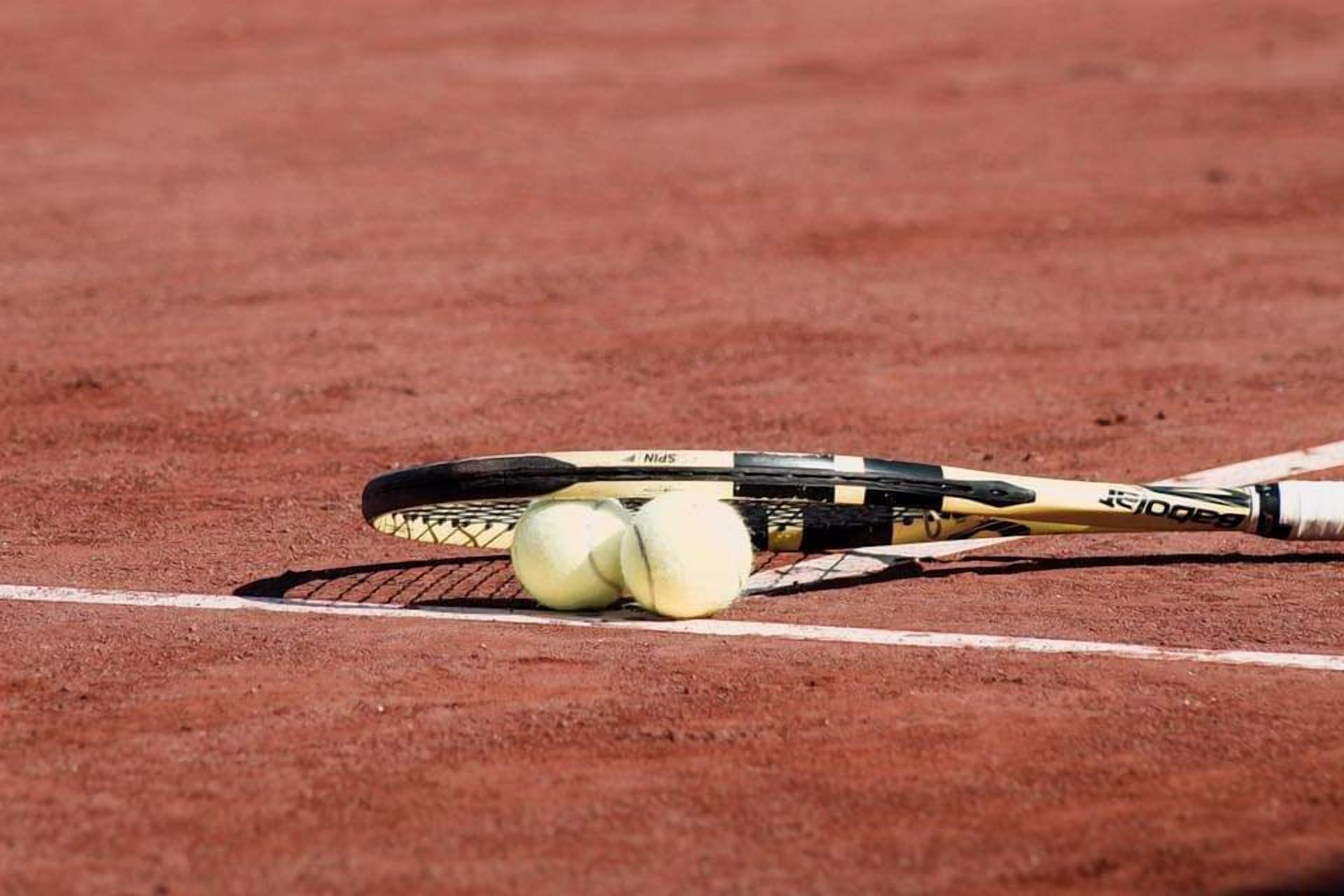 Une raquette de tennis et deux balles de tennis sur un court en terre battue.