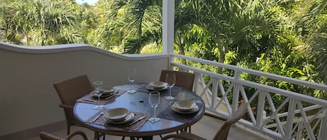 Una mesa redonda con cuatro sillas, dispuesta con platos, tazones y copas de vino, rodeada por una barandilla blanca en un balcón con vistas a densa vegetación.