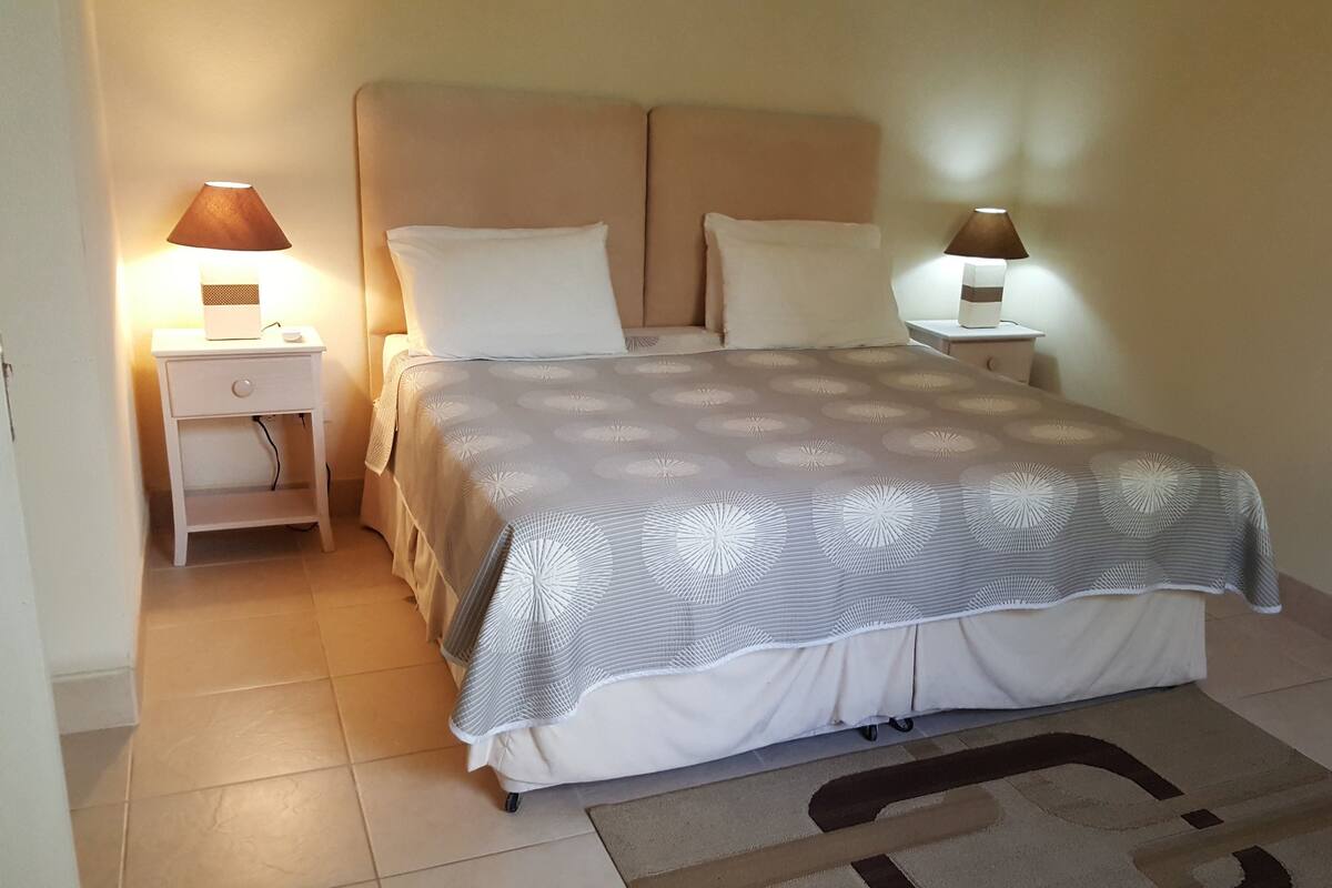 Una cama bien hecha con un edredón estampado, dos lámparas de noche y una mesita de noche con una lámpara.