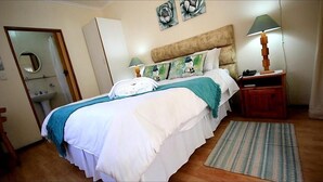 A neatly made bed with a white and teal bedspread, a wooden headboard, and a bedside table with a lamp. - Dove's Nest Guest House (Kempton Park)