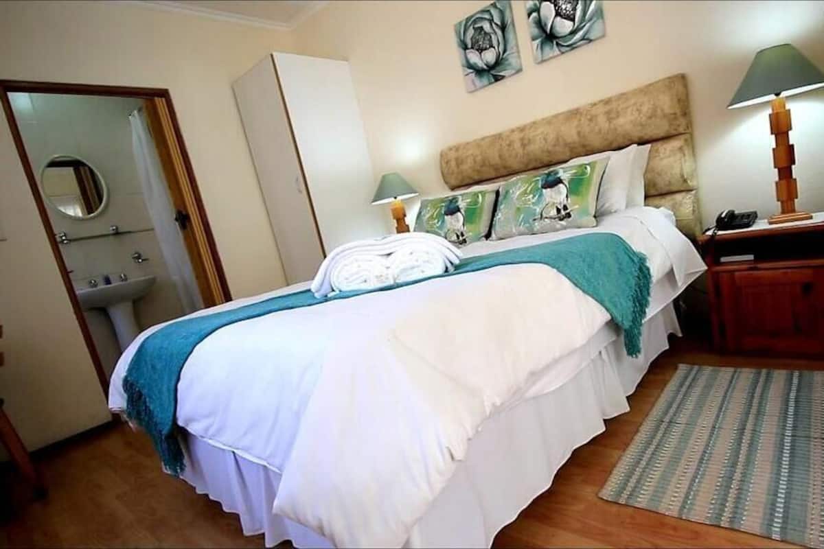 A neatly made bed with a white and teal bedspread, a wooden headboard, and a bedside table with a lamp.