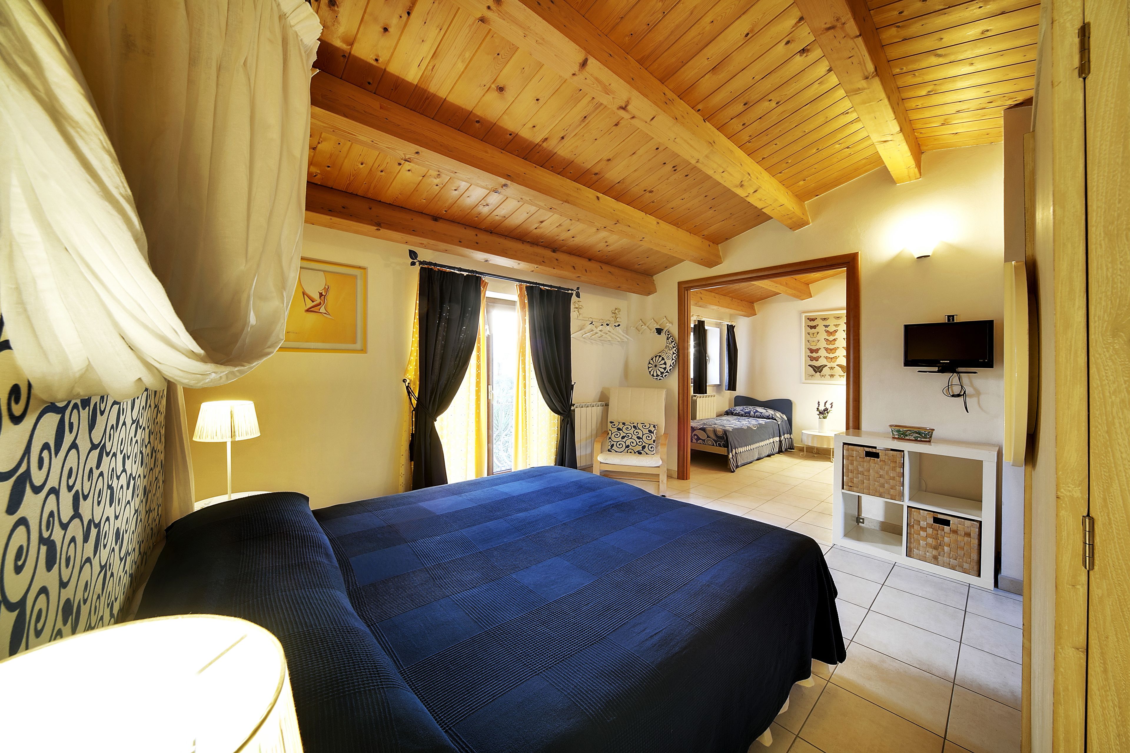 A bedroom with a large bed, wooden ceiling beams, a television, and a small cabinet.
