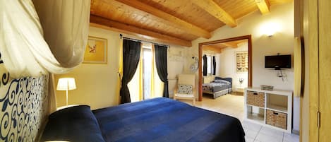 A bedroom with a large bed, wooden ceiling beams, a television, and a small cabinet.