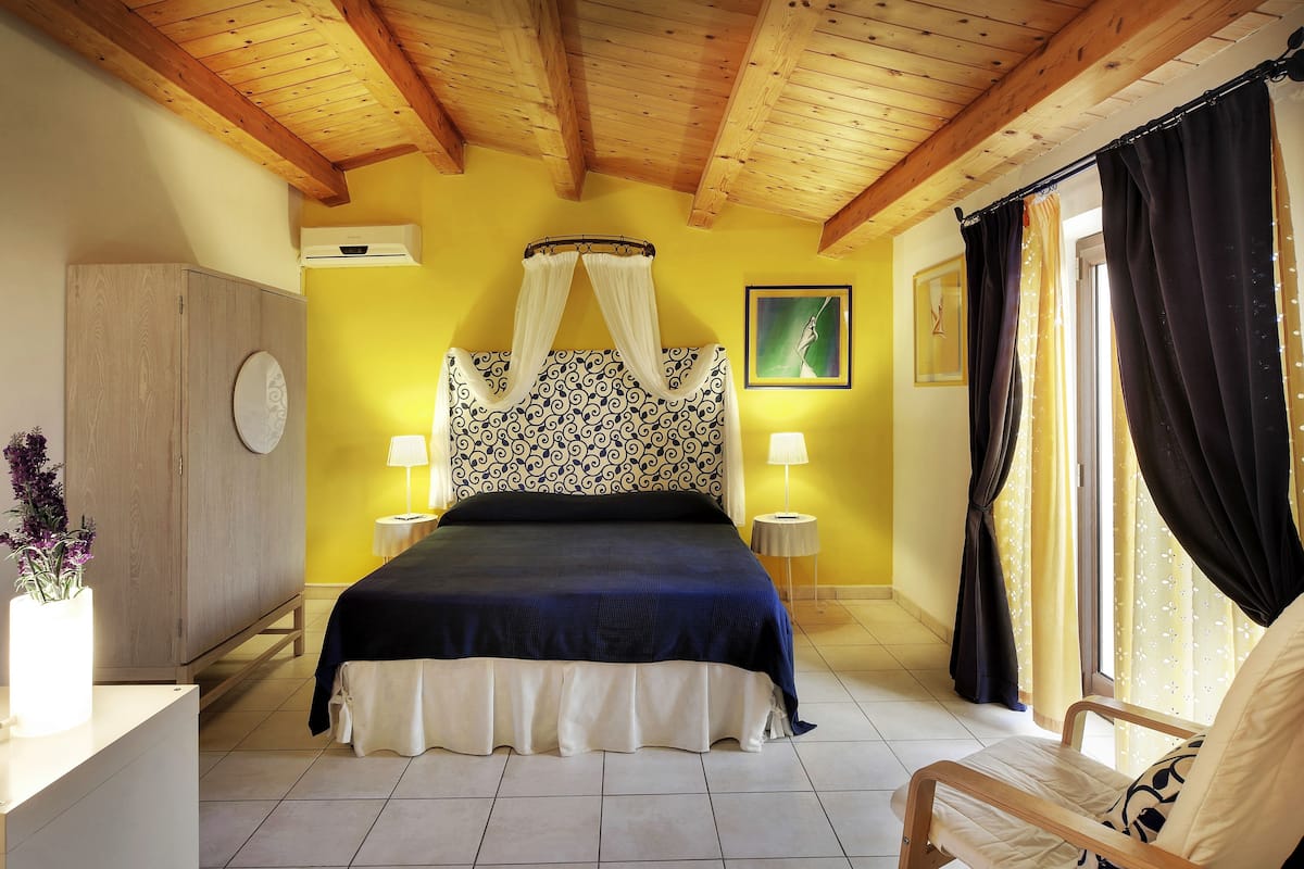 Ein Schlafzimmer mit Bett, Nachttischlampen, einem Nachttisch, einem Sessel und einem Fenster mit Vorhängen.