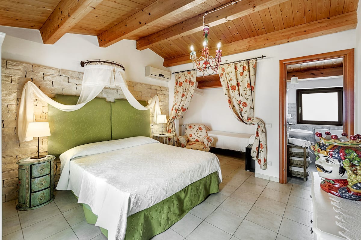 Ein Schlafzimmer mit grünem Kopfteil, einem Himmelbett, einer Kristallleuchtre, einem blumigen Sessel und einer traditionellen Tür.