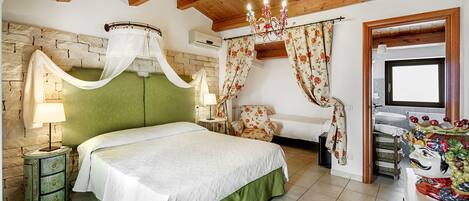 A bedroom with a green headboard, a four-poster bed, a chandelier, a floral chair, and a traditional door.