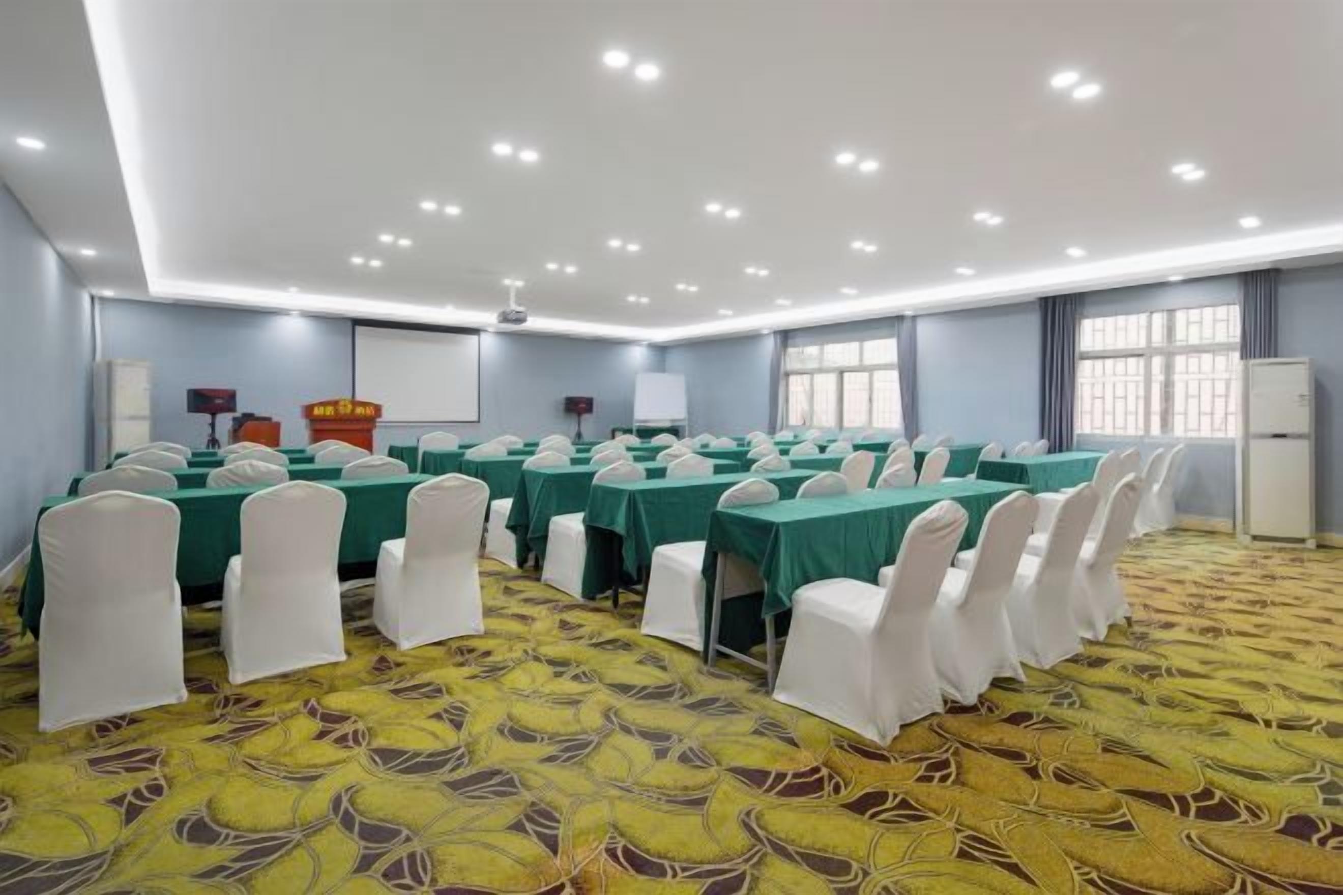 Un salón de conferencias con mesas, sillas, un atril y una pantalla para proyector.