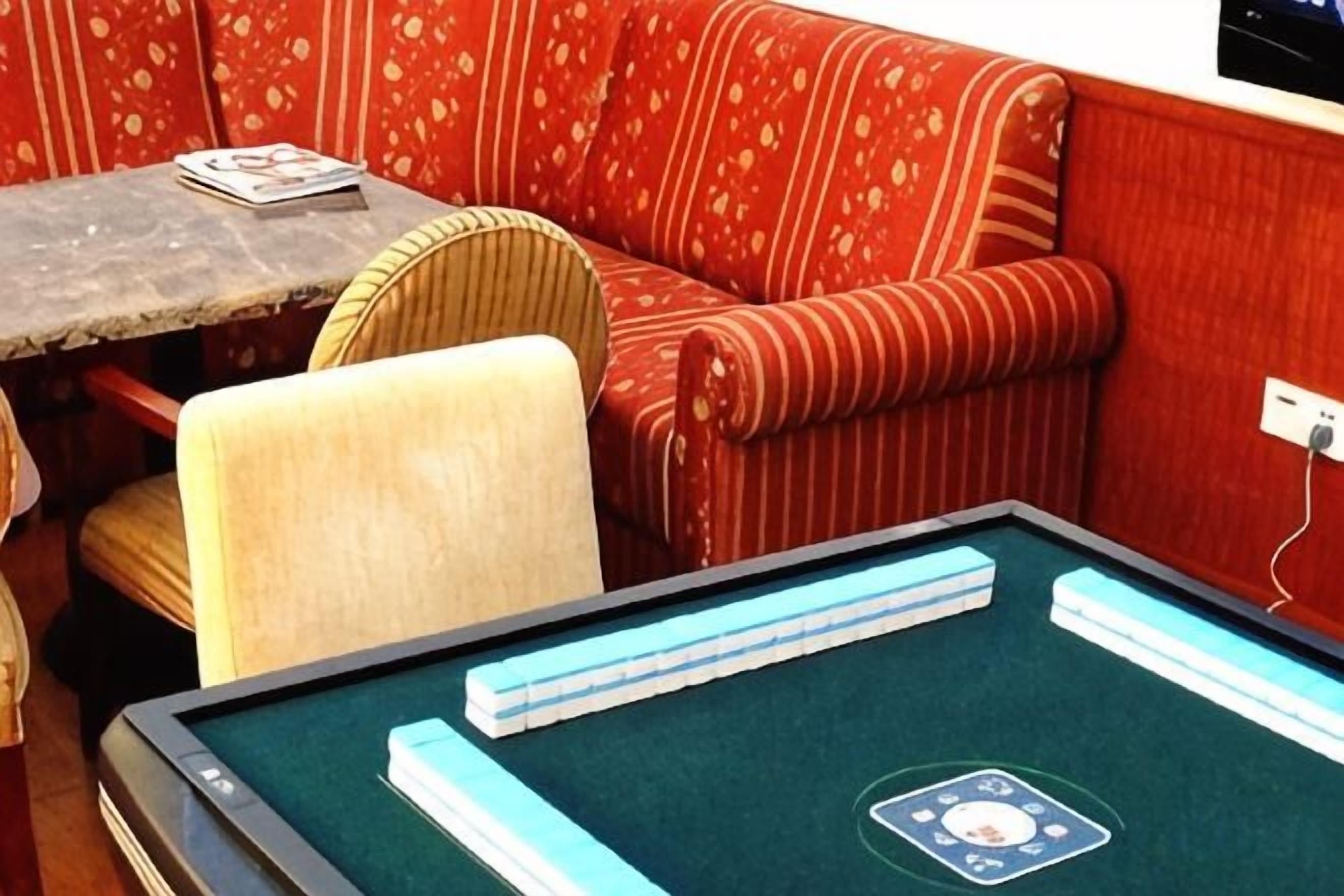 Una habitación con mesa de billar, un sofá rojo con estampado y una mesita con una revista.