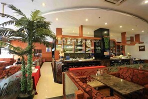 Un restaurante con cabinas y mesas, una zona de bar y una planta grande en maceta.