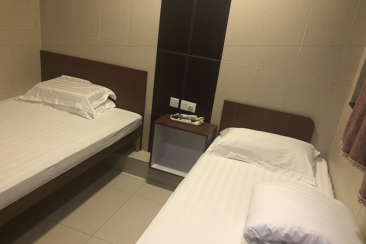 A hotel room with two single beds, a small bedside table with a phone and a lamp, and a wall-mounted shelf.