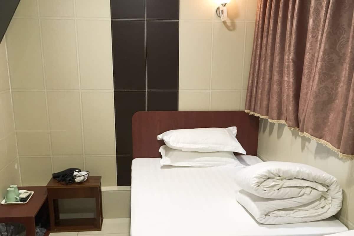A hotel room with two beds, a small table with a trash bin, and a wall-mounted light.