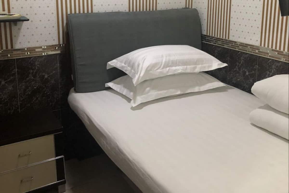 A neatly made bed with white bedding, a dark headboard, and a small bedside table with drawers.