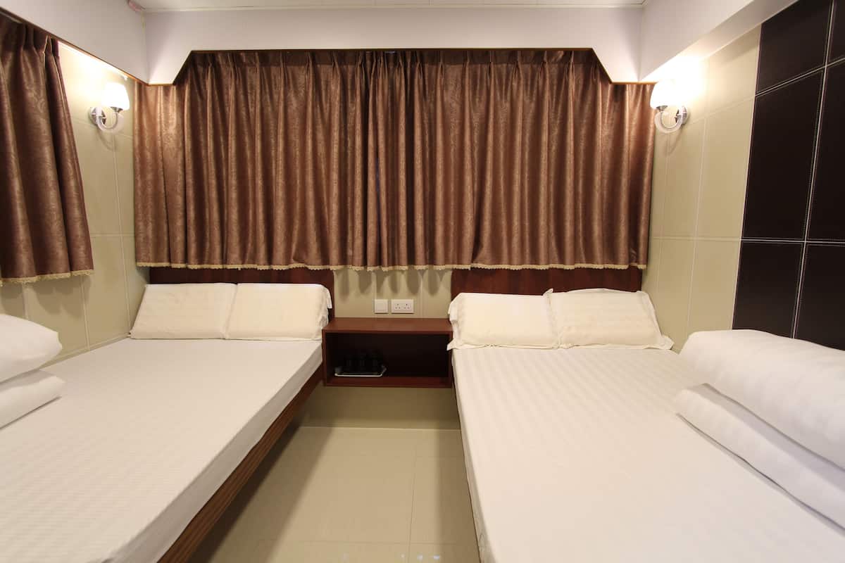 A hotel room with two beds, a nightstand, and a large window with brown curtains.