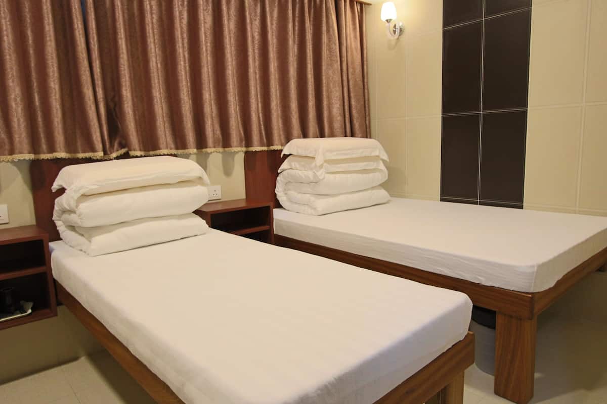 Two single beds with white linens, wooden headboards, and a wall-mounted light fixture.