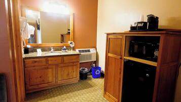 A bathroom with wooden cabinets, a sink, a mirror, a trash bin, and a microwave.