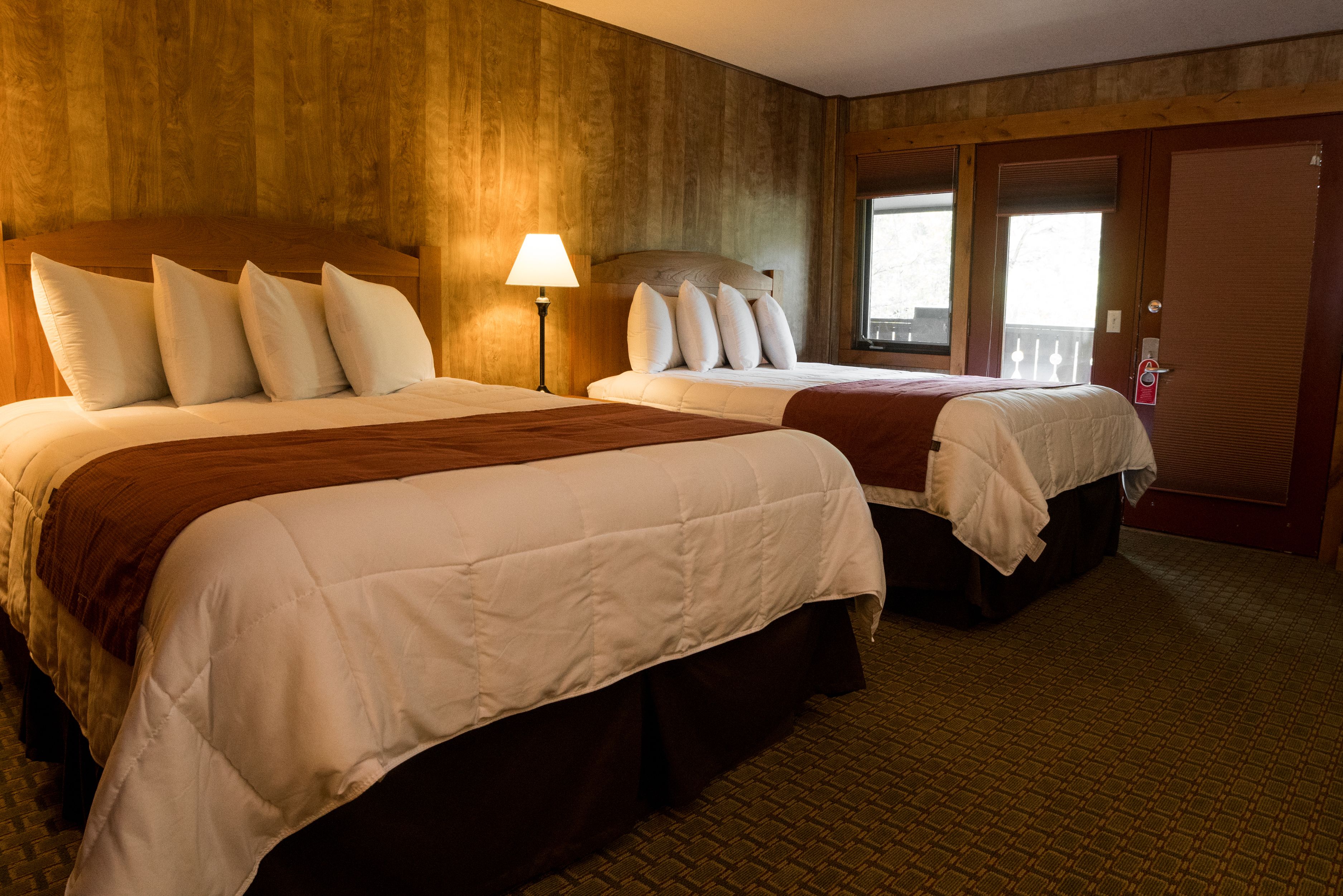 Een hotelkamer met twee bedden, houten lambrisering, een raam met uitzicht en een deur met een handgreep.
