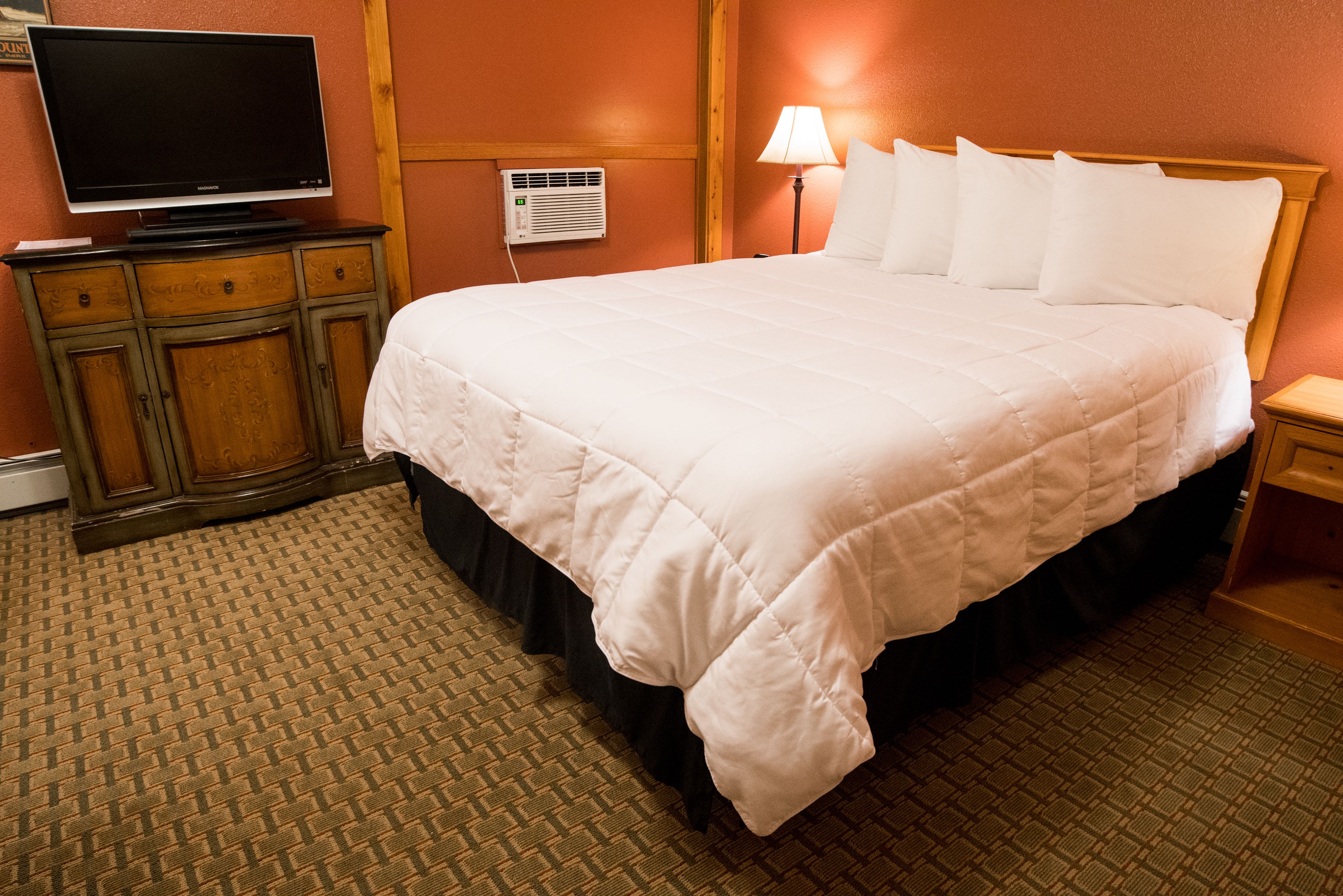 Habitación de hotel con una cama grande, un televisor sobre un mueble de madera, un aire acondicionado instalado en la pared y una lámpara de noche.