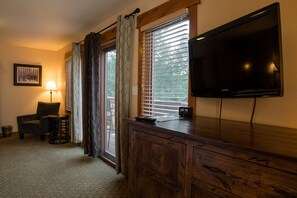 A room with a wooden desk, a television, a chair, a lamp, and a window with blinds.