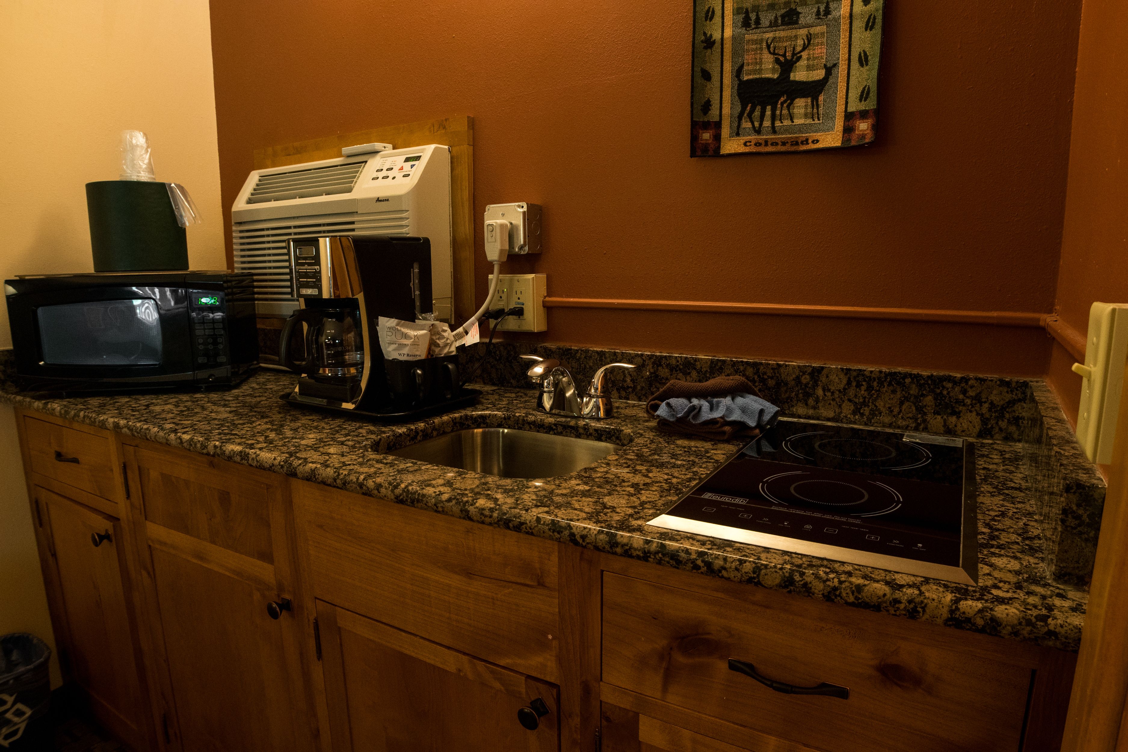 Una cocina con encimeras de granito, microondas, cafetera, fregadero y estufa.