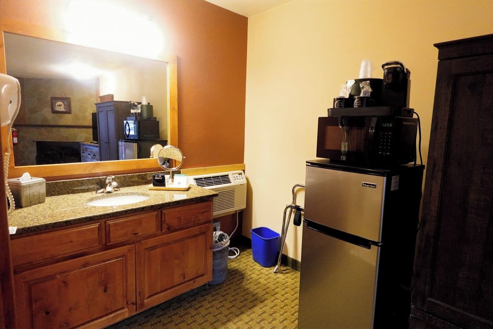 A hotel bathroom with a granite countertop sink, a mirror, a microwave, and a refrigerator.