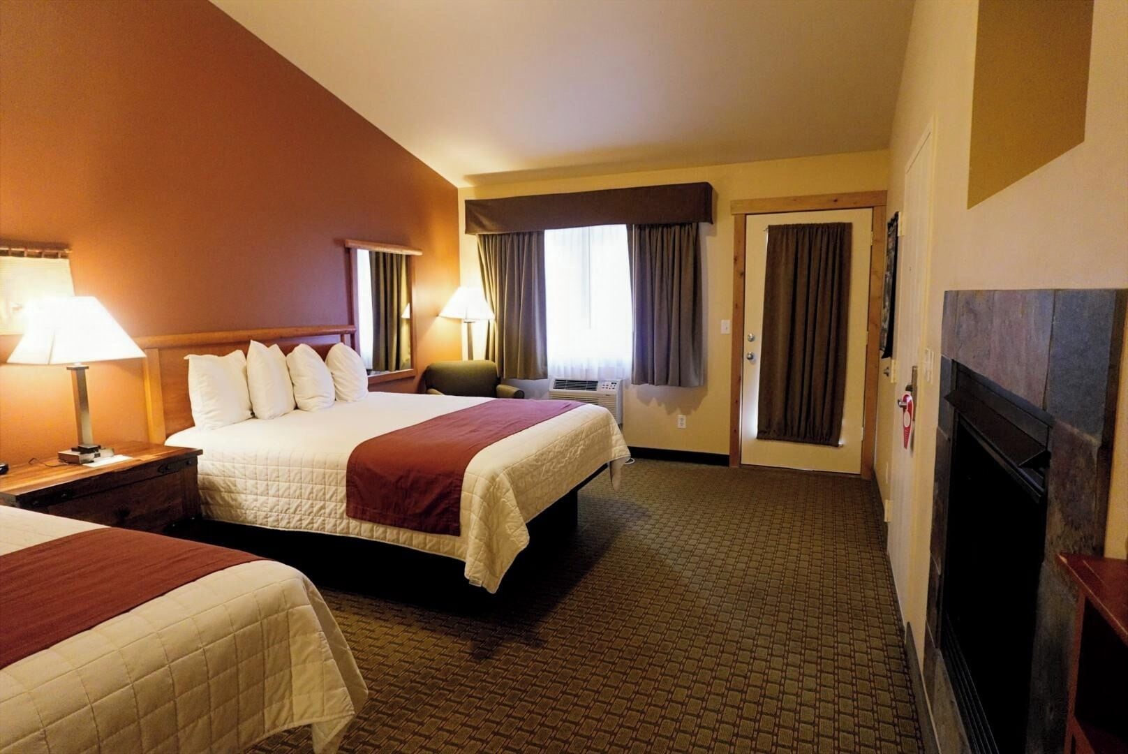 Une chambre d’hôtel avec deux lits, une cheminée et une grande fenêtre avec des rideaux.
