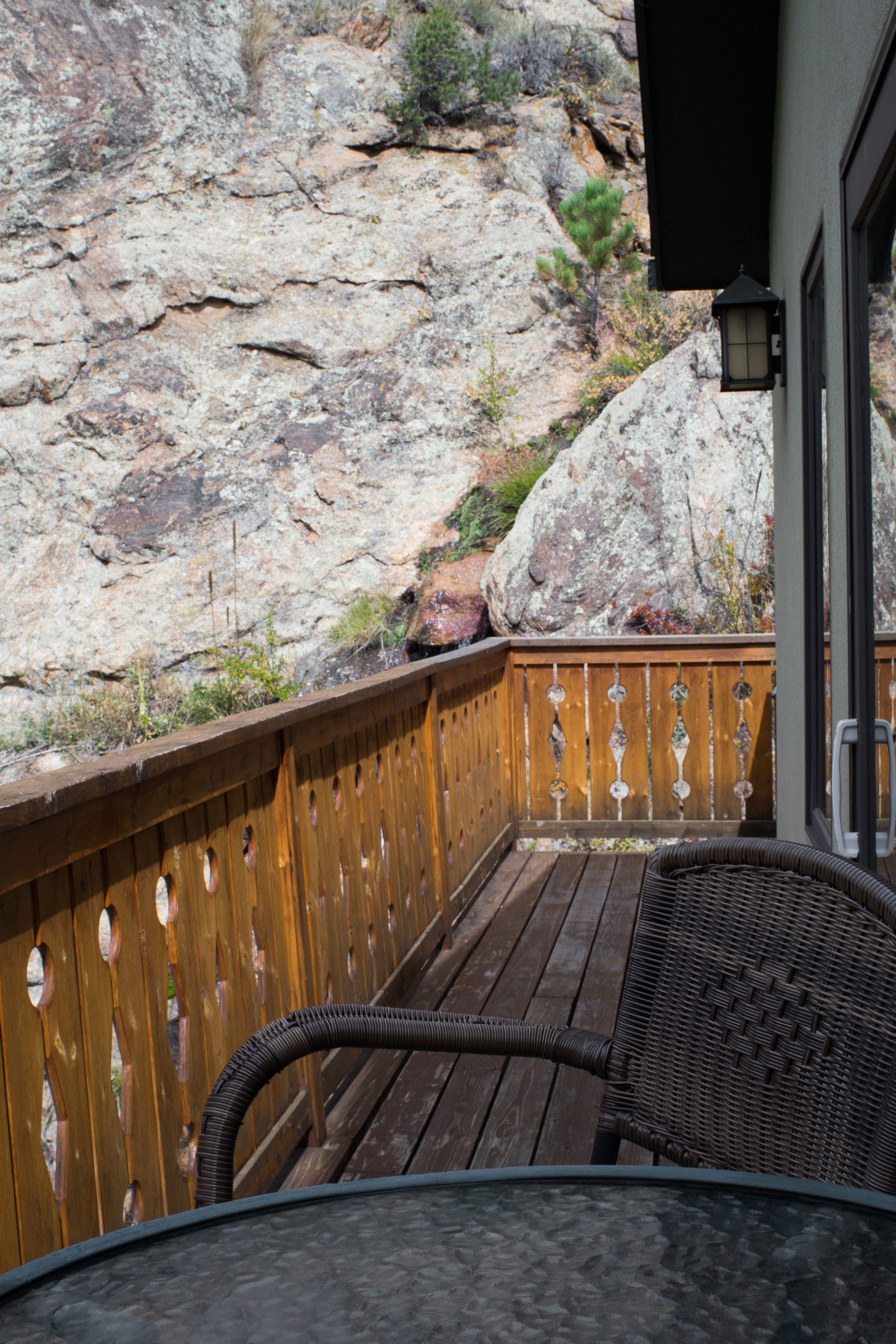 A wooden deck with a wicker chair and a table, overlooking a rocky landscape.