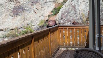 A wooden deck with a wicker chair and a table, overlooking a rocky landscape.