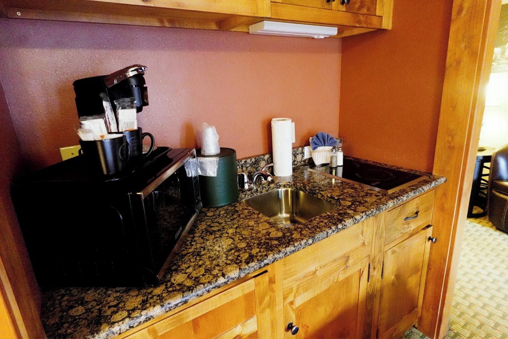 A kitchen with a granite countertop, a coffee maker, a microwave, a sink, and wooden cabinets.