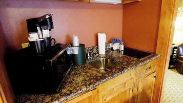 Una cocina con encimera de granito, cafetera, microondas, pileta y muebles de madera.