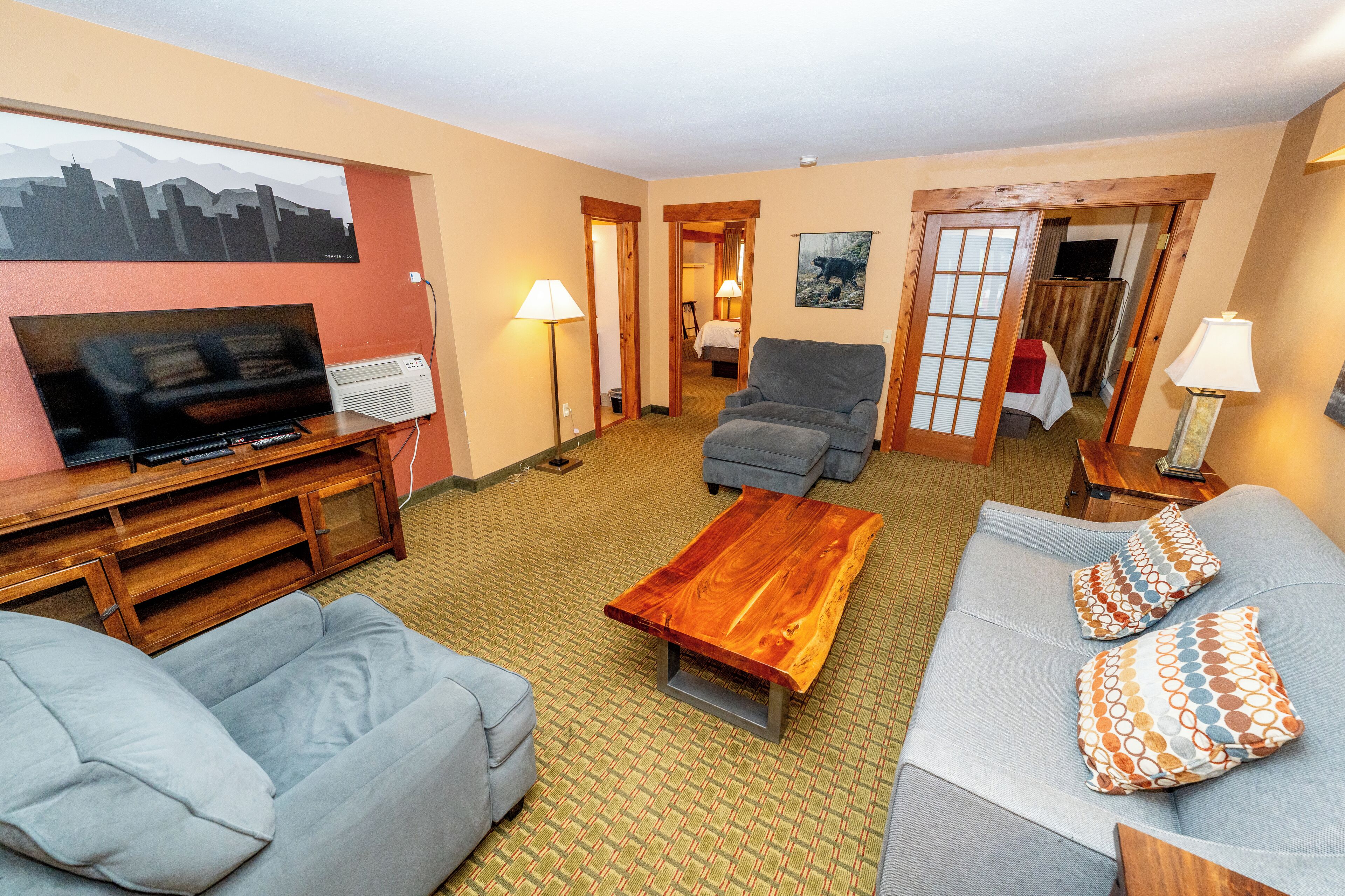 A hotel room with a TV, sofa, armchair, and a wooden coffee table.