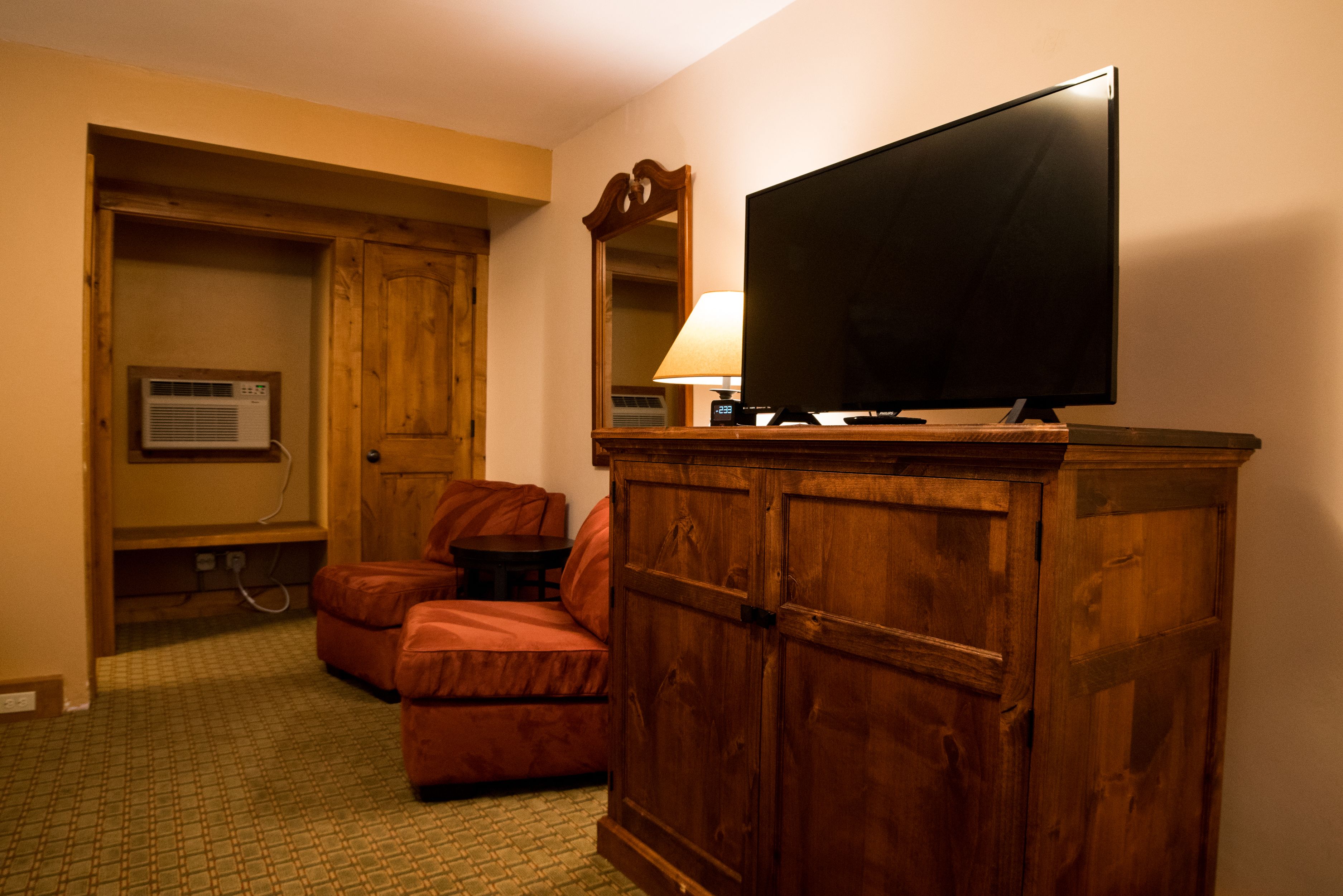 A hotel room with a wooden cabinet, a television, a lamp, and a seating area with a sofa and armchair.