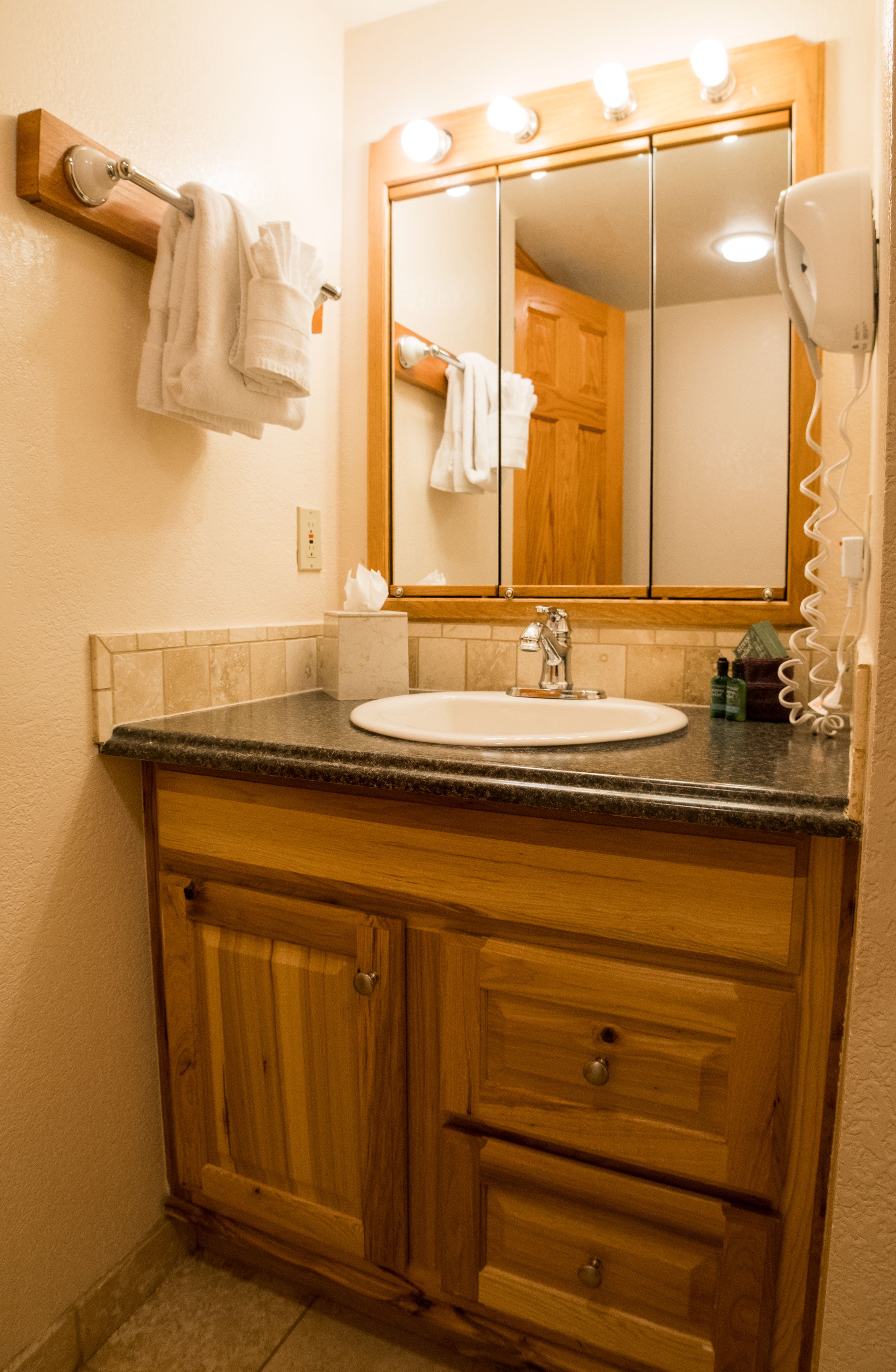 A bathroom with a wooden vanity, a sink, a mirror, and a hairdryer.