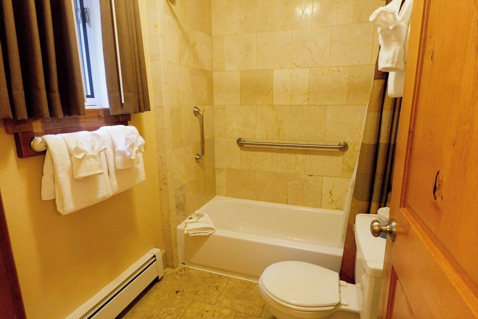 A bathroom with a bathtub, toilet, and a towel rack with towels.