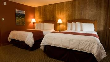 A hotel room with two beds, each with a white bedspread and a brown skirt. There are two bedside lamps and a painting on the wall.