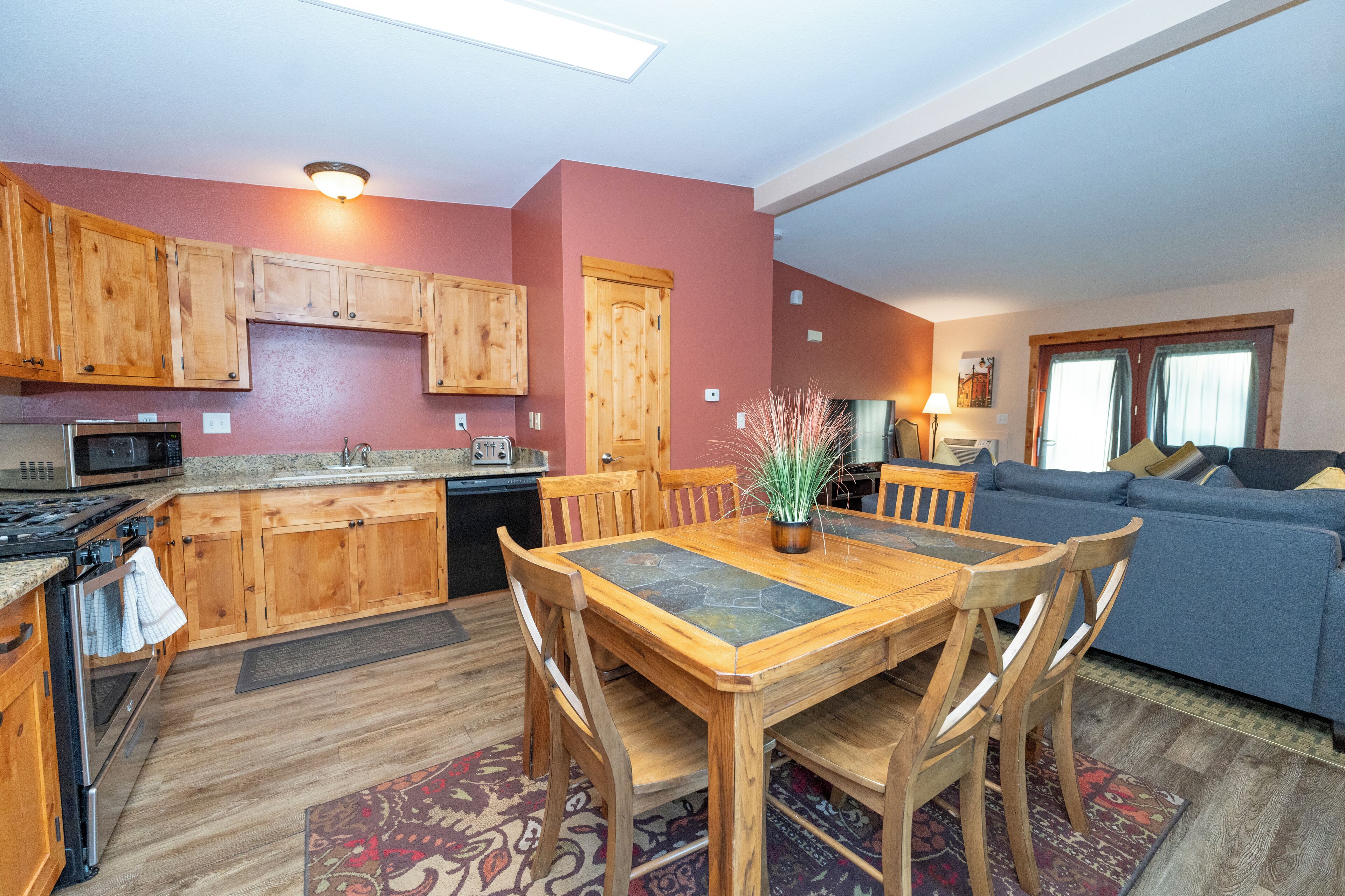 A kitchen with wooden cabinets, a dining table with chairs, a microwave, and a stove.