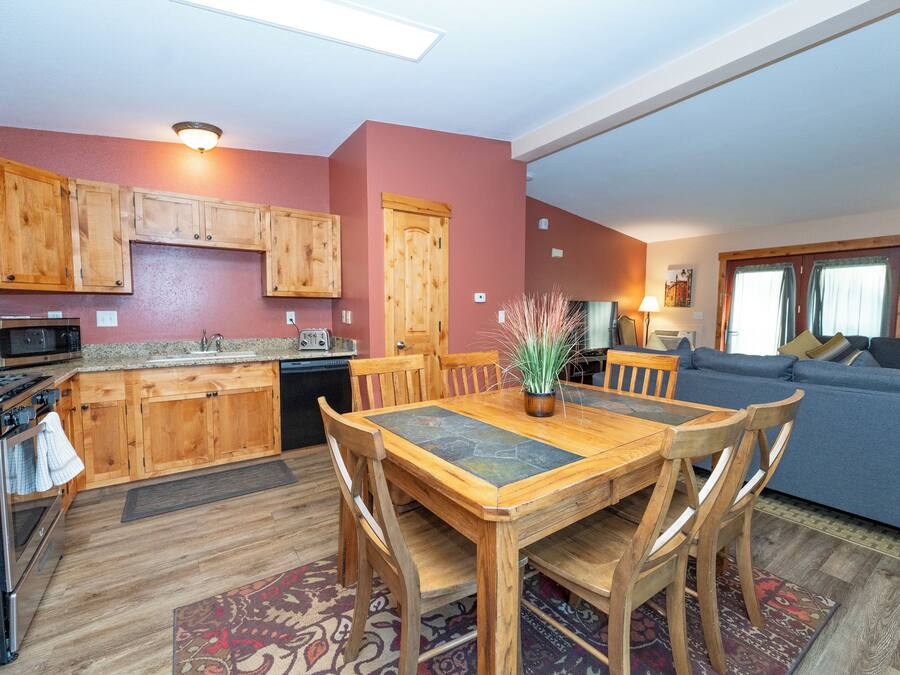 A kitchen with wooden cabinets, a dining table with chairs, a microwave, and a stove.
