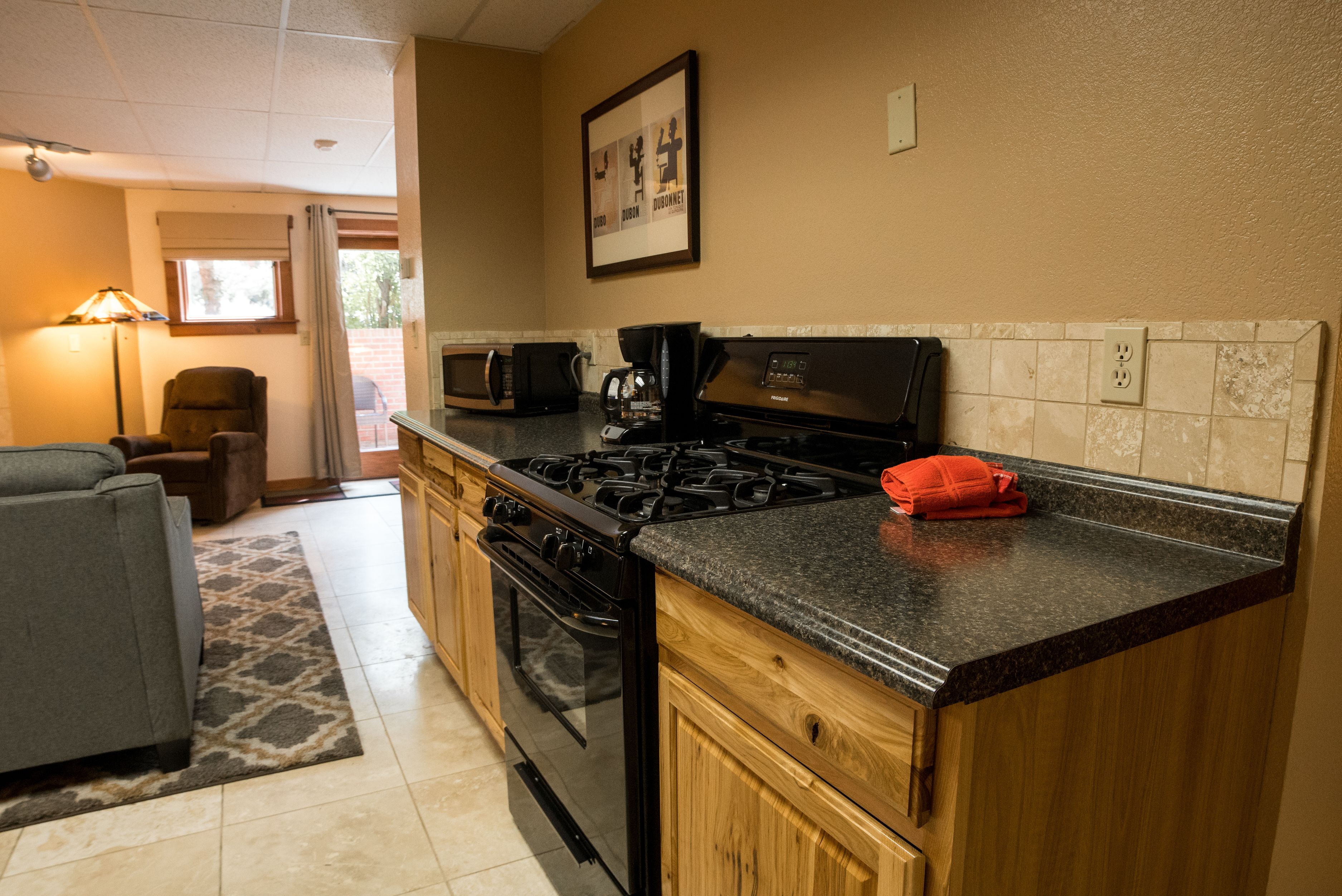 A kitchen with a stove, microwave, and oven. There is a chair and a couch in the adjacent living area.