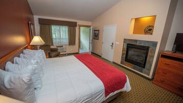 A hotel room with a large bed, a fireplace, a desk with a lamp, and a door leading to another room.