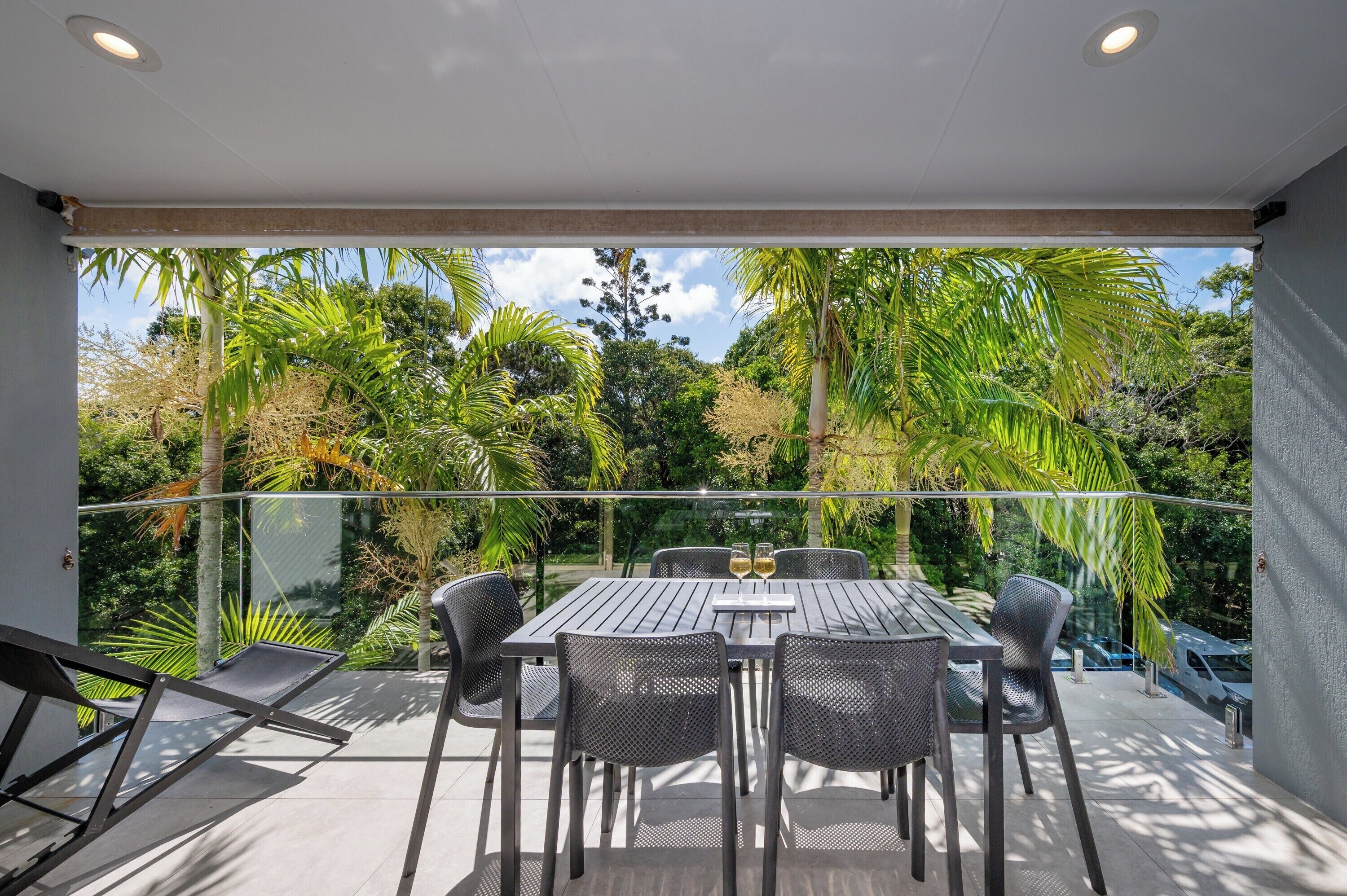 A balcony with a table and chairs, overlooking a lush garden with palm trees and other greenery.